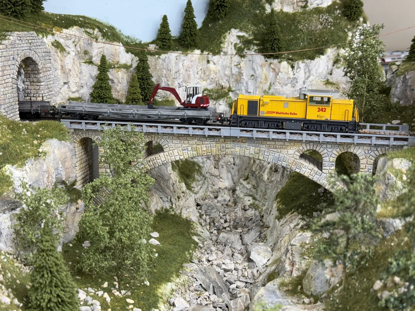 Yellow RhB engineering train crossing a high stone viaduct