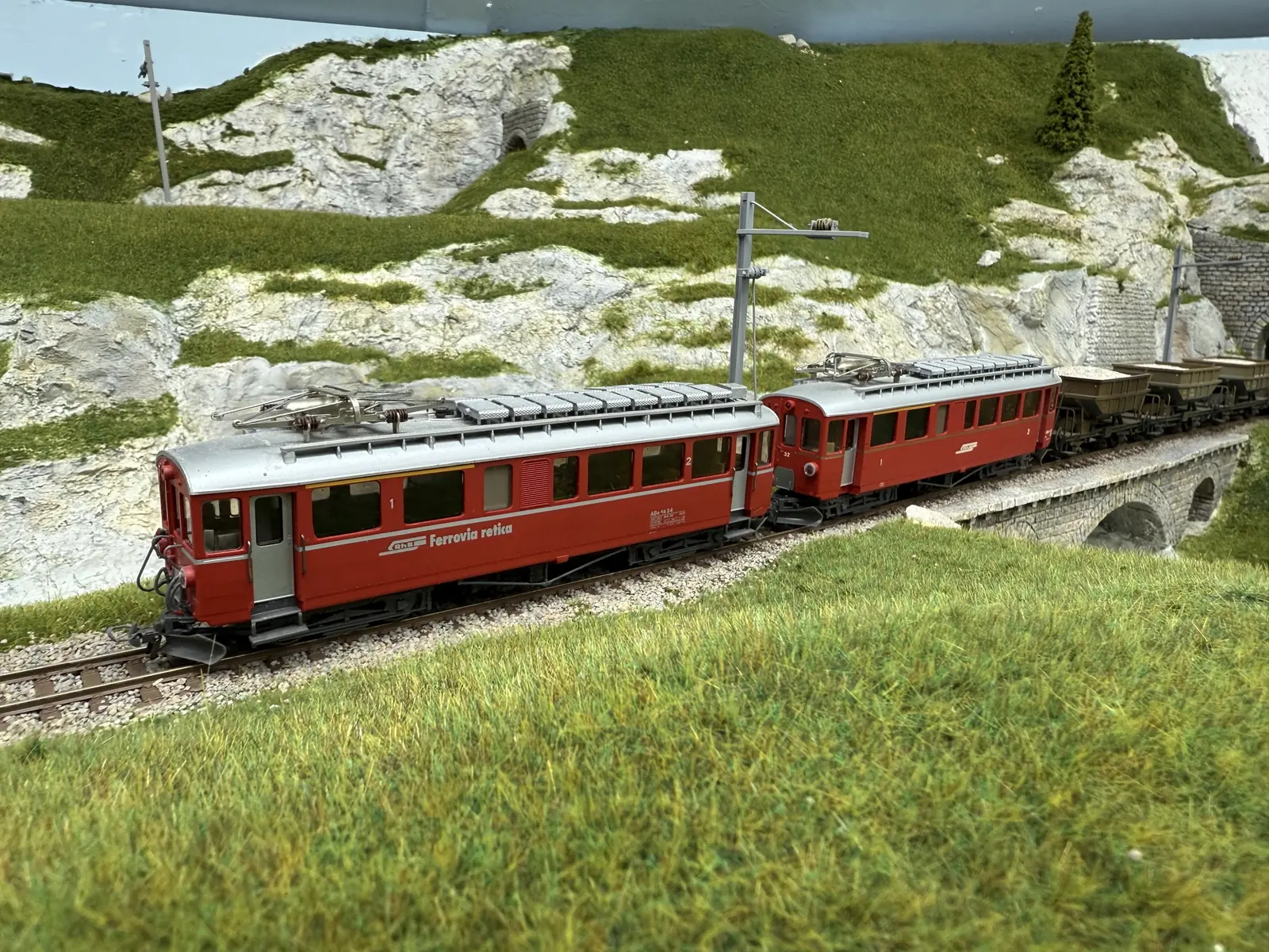 Red RhB passenger train travelling through the model Alpine landscape
